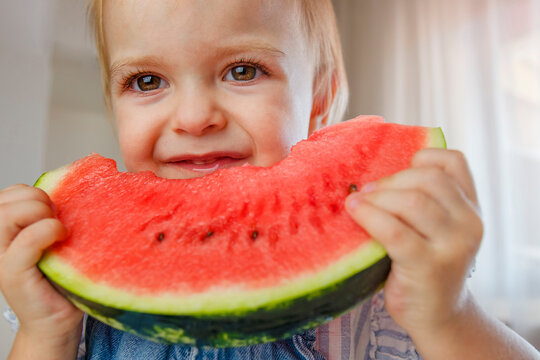 Little child with big red slice of watermelon sitting on highchair. Healthy eating concept. Healthy food at home