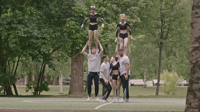 Wide shot of cheerleading squad practicing pyramid stunt while training together on outdoor sports field