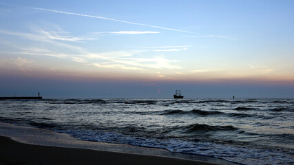 Scenic sunset over the sea. Touristic ship sailing through the sea. Poland seaside, Leba village and beach. Seascape