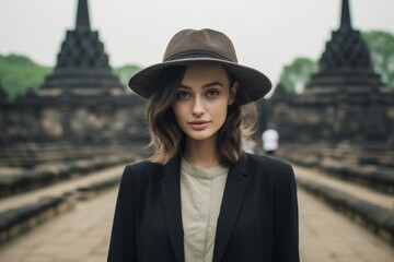 Lifestyle portrait photography of a tender girl in her 20s wearing a formal top hat at the borobudur temple in magelang indonesia. With generative AI technology