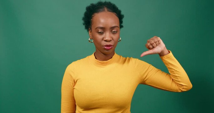Beautiful young woman gives single thumbs down, green studio background