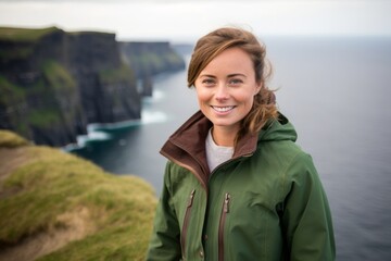 Environmental portrait photography of a jovial girl in her 40s wearing a stylish varsity jacket at the cliffs of moher in county clare ireland. With generative AI technology - obrazy, fototapety, plakaty