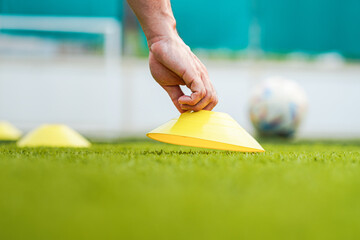 Action of a trainer hand is placing an obstacle cone on turf ground for preparing the speed...