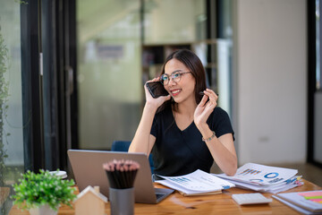 Businesswoman using laptop to work and calling colleagues or clients via mobile phone.