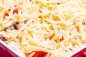 Raw casserole with potatoes, sausage and colorful bell pepper, closeup in baking dish, horizontal