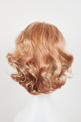 Fototapeta premium Natural looking blonde fair wig on white mannequin head. Short hair cut on the plastic wig holder isolated on white background, back view.