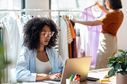 Smart beautiful fashion designer working with laptop of new collection of clothes in the sewing workshop. - Powered by Adobe