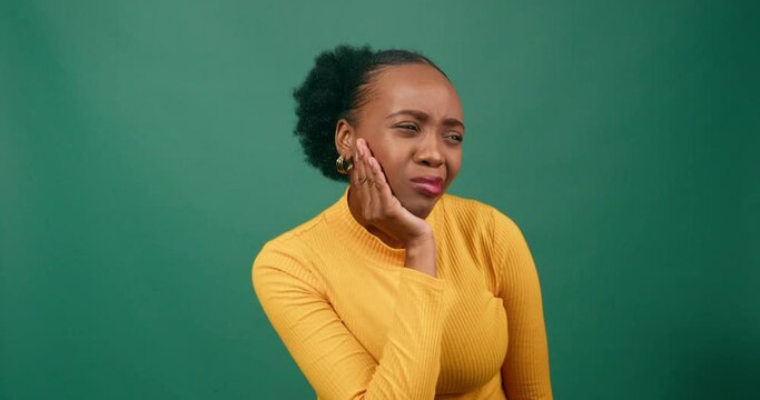 Young Black woman rubs jaw in pain, toothache, studio green background orange