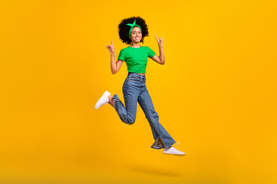 Full body portrait of beautiful excited teen schoolgirl jump hands fingers show heavy metal symbol isolated on yellow color background