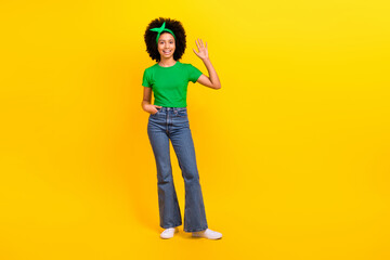 Full length portrait of friendly cute cheerful girl arm palm waving hi empty space ad isolated on yellow color background