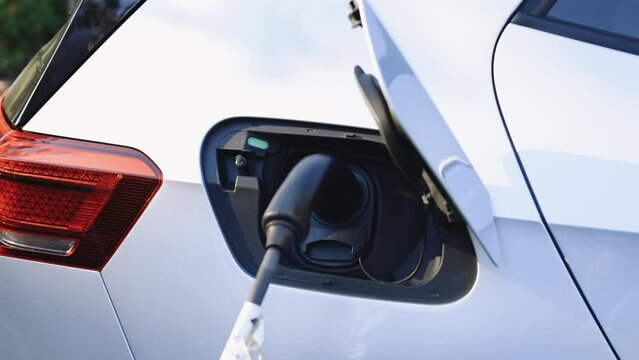 Electric vehicle charging port plugging in EV modern car. Modern electric car charging battery with power cable on parking lot in the city street. Save ecology alternative energy sustainable of future