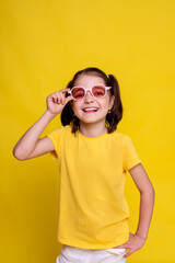 excited child in mockup yellow T-shirt in pink retro sunglasses and looking at camera on yellow background. studio advertising photoshoot