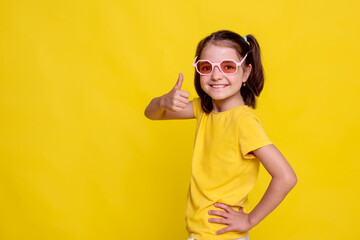 child girl in mockup yellow T-shirt with thumb up and looking at camera on yellow background. studio advertising photoshoot