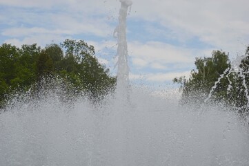 Fountain water jets on a summer day against the backdrop of green trees and blue sky.