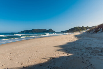 Morro das Pedras beach with waves. Sandy coastline with sky and sun light in Brazil