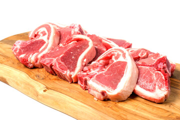 Stack of fresh lamb loin chops on wooden cutting board and on white surface. Premium high quality red meat. Butcher craft. Uncooked product.