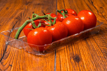 Fresh ripe tomato on a vine in plastic tray on wooden table surface. Organic product. Food supply chain industry. High quality vegetable.