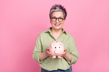 Photo of positive successful businesswoman elderly wear trendy khaki shirt hold piggy bank collect...