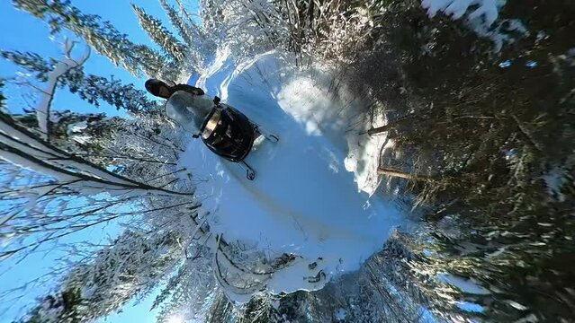 Somewhat goofy looking 360-degree tiny planet clip of a person on a snow machine riding down a trail through an evergreen forest. The sun flickers between the trees.
