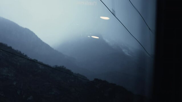Window POV of passenger looking at electric wires passing by with mountains and fog in background. traveling by train