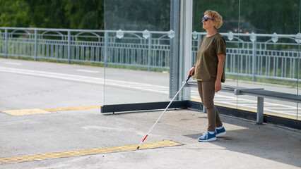 An elderly blind woman is waiting for transport at a bus stop.