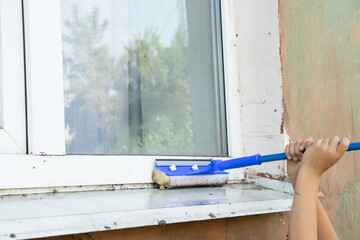 A child washes a dirty window with a mop from the street