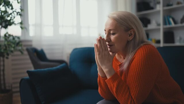 Hopeful middle-aged woman praying at home, asking God for help, Christianity