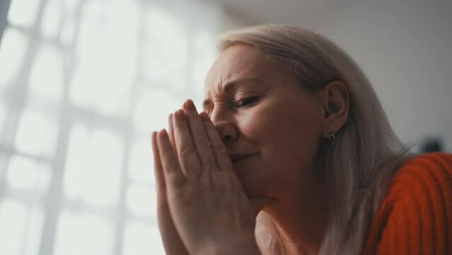 Woman in her 50s praying at home, putting hands together, asking God for mercy
