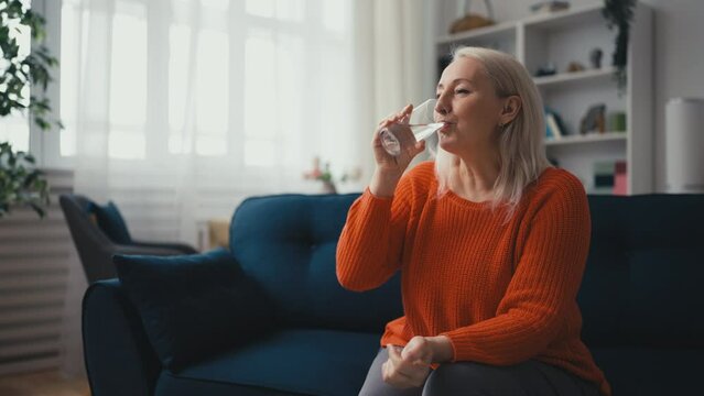 Cheerful middle aged female taking vitamins with water and smiling, healthcare