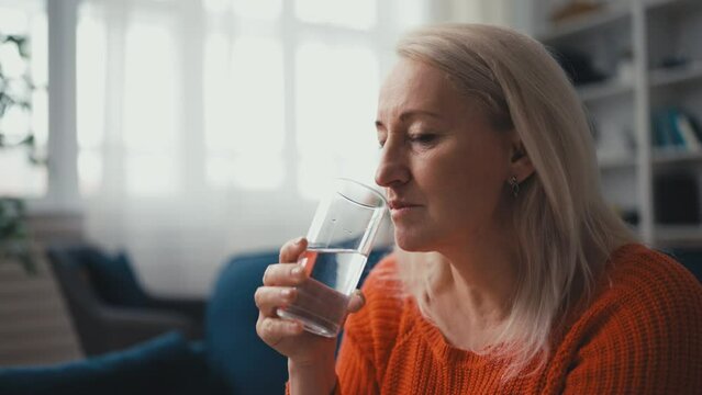 Unhappy middle-aged woman taking medication with water, painkillers or vitamins