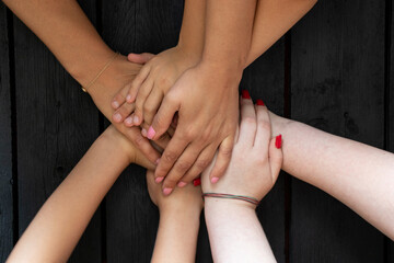 Female hands and child's hands on a wooden black board as a team, strength and unity of the family, many hands