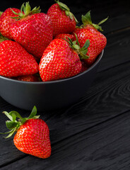 Strawberry in the  black bowl on the black wooden background. Closeup.