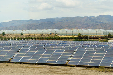 Solar panels of the power plant against the backdrop of greenhouses and mountains.