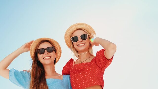 Two young beautiful smiling hipster women in trendy summer same clothes. Carefree models posing in the street. Positive models having fun. Cheerful and happy, at sunny day. In hat and sunglasses