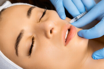 Young beautiful woman gets injection of botox in her lips for lip augmentation by cosmetologist in...