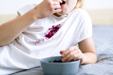 The child eating berries while sitting on the bed. Dirty blueberry stain on white clothing. daily life stain concept.