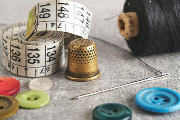 Sewing kit of needle, thimble, thread and measuring meter.On gray concrete table top.