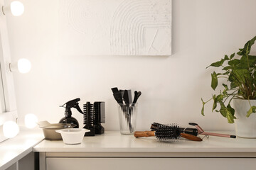 Different hairdressing tools on table near light wall