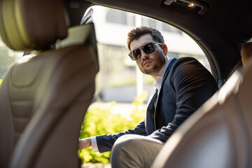 Handsome businessman getting in the car on backseat of luxury taxi. Vehicle transportation and business lifestyle concept