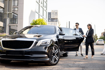 Female chauffeur helps a business man to get out of the car. opening a door. Concept of personal driver, luxury taxi or business trips - obrazy, fototapety, plakaty