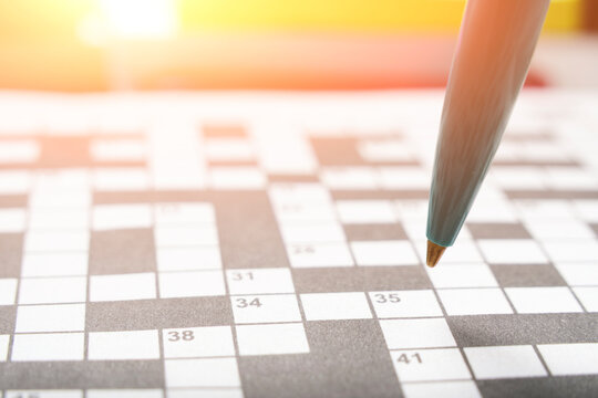 Ballpoint pen on background crossword puzzle sheet in the contoured sunlight.