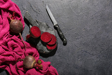 Wooden cutting board with beet and knife on black background