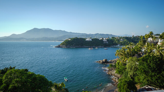 Hermoso paisaje de la playa en el mar con cerros y monta&ntilde;as de fondo con rocas y piedras en la costa a la orilla del agua azul con frondosos &aacute;rboles con un cielo azul en Manzanillo Colima M&eacute;xico