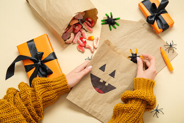 Woman packing different Halloween candies on beige background