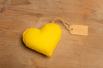 Un corazón amarillo hecho de tela con una etiqueta e blanco sobre un fondo de madera rústico. Vista superior y de cerca. Copy space