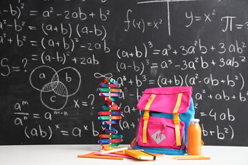Pink school backpack with stationery, molecular model and bottle of juice on white table near black...