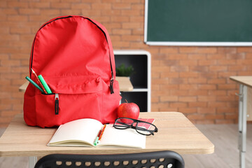 Red school backpack with stationery on desk in classroom