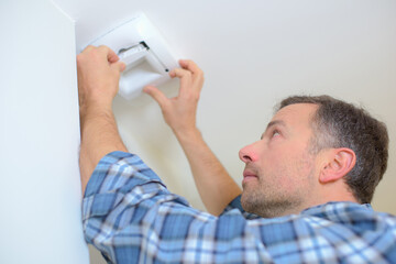 worker installing smoke detector on the ceiling