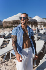 Chico joven tatuado y musculoso posando en verano en playa soleada