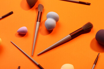 Makeup sponges and brushes on orange background